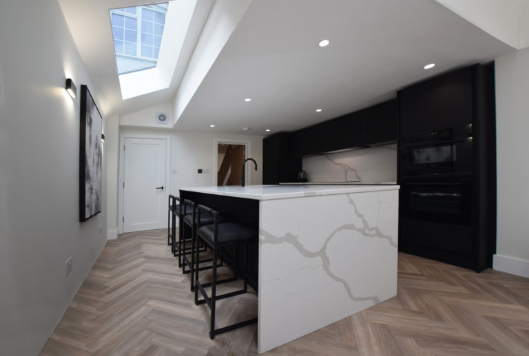 A tastefully designed kitchen extension within a Victorian terrace. The interior showcases a modern ambiance with contrasting black and white tones, complemented by wooden flooring.