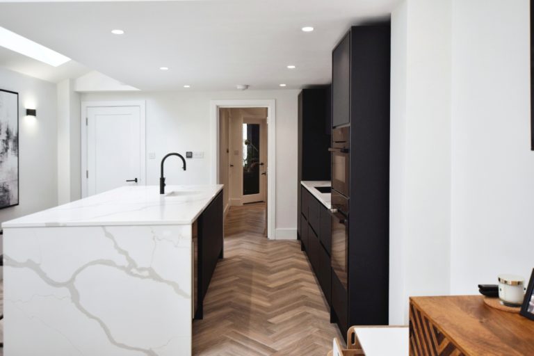 A contemporary kitchen-dining space in a Victorian home. The interior design incorporates black and white accents with a stylish island and wooden flooring.