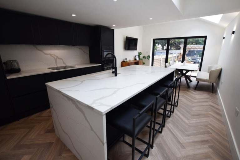 A spacious modern kitchen extension in a Victorian terraced property. The image showcases a sleek black and white color scheme with a prominent island and timber flooring.